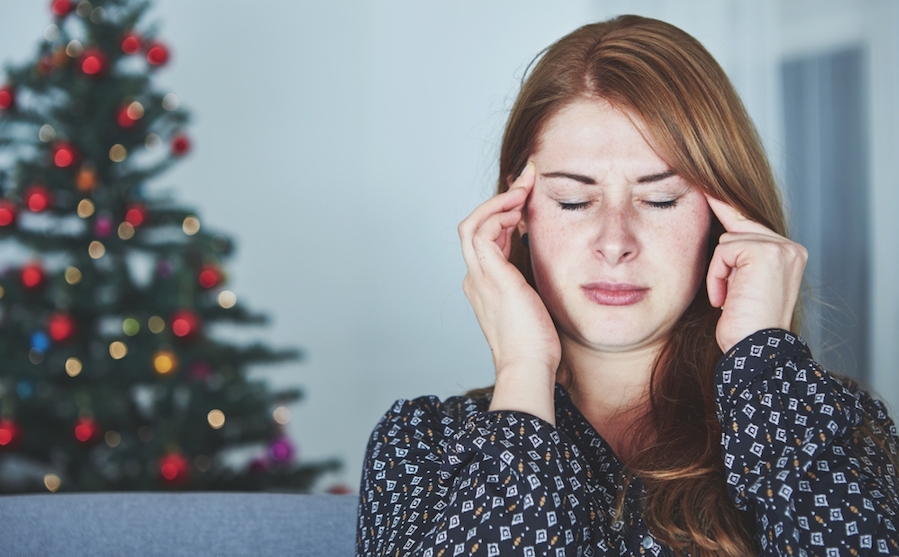 A highly sensitive person holding her hands to her head to deal with holiday stress in front of a Christmas tree