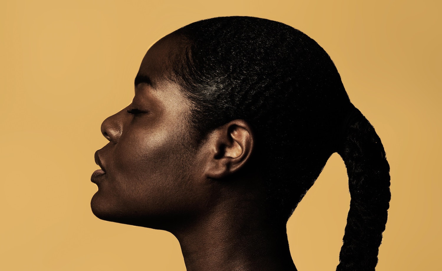 A strong, powerful Black woman in profile against a yellow background, with a sensitive expression on her face.