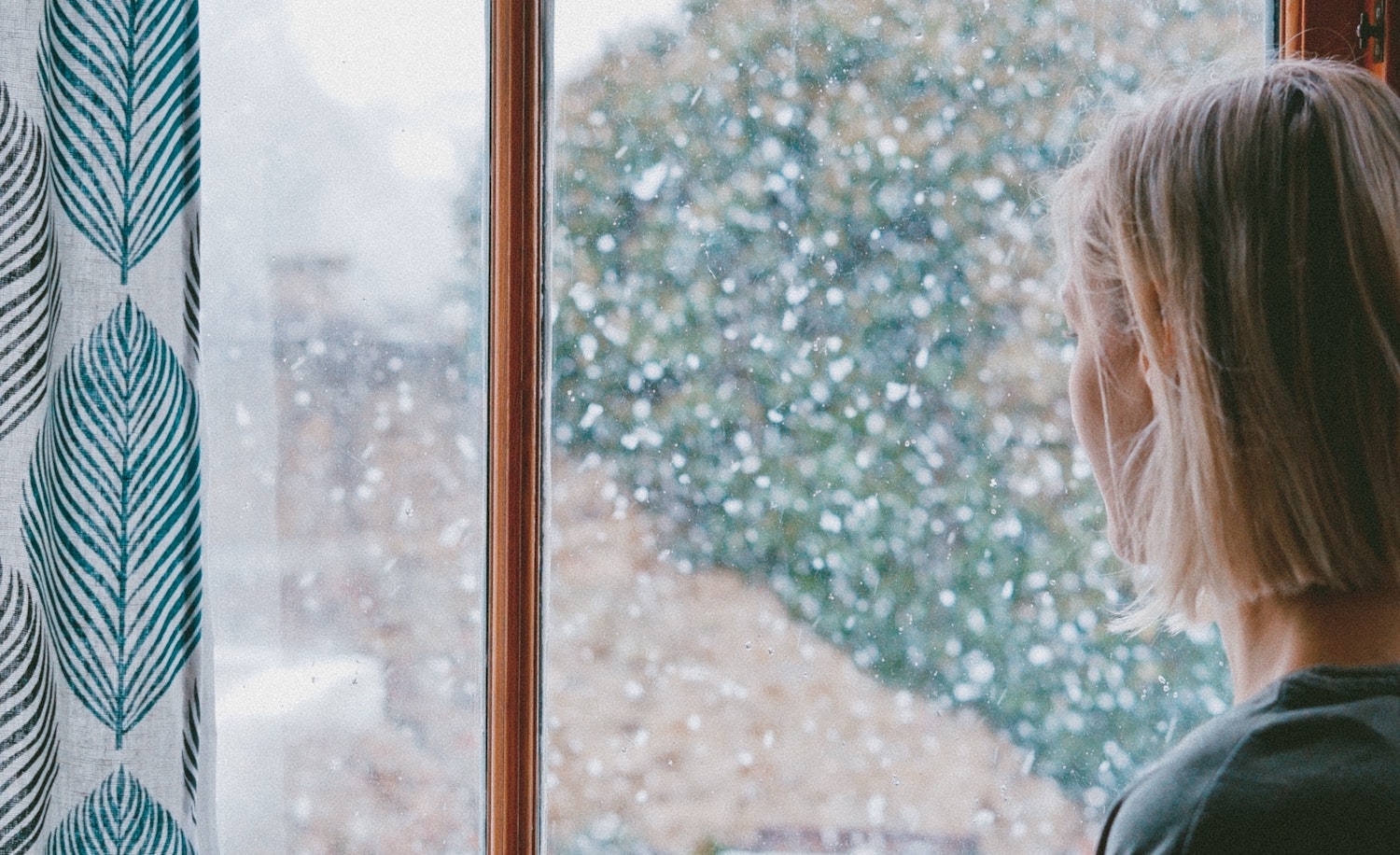 A highly sensitive person with seasonal affective disorder looks out the window at snow falling and appears sad.