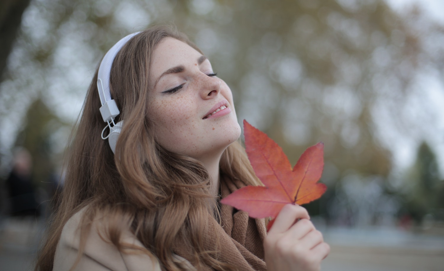 A sensitive person (woman) beaming with a big happy smile and holding an autumn leaf to her face.