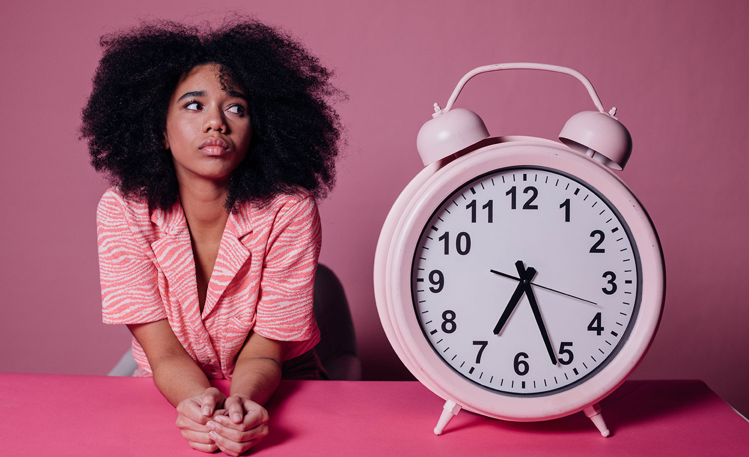 A stressed-out woman next to a big pink clock.
