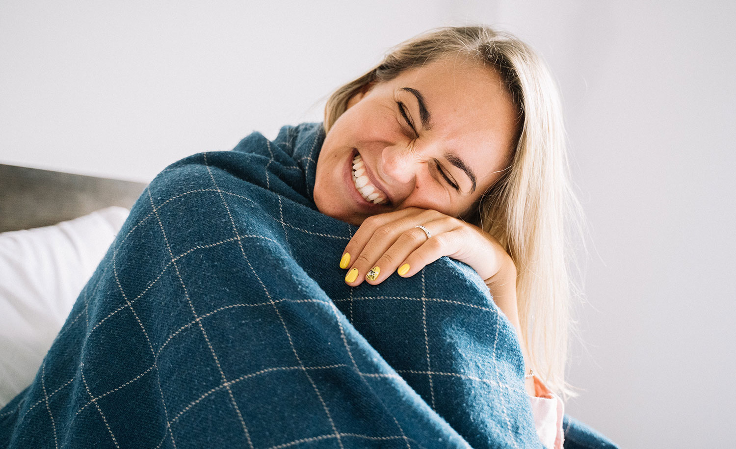 A happy highly sensitive woman cozied up in a blue blanket