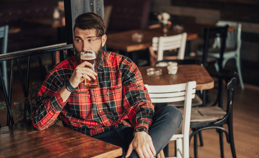 A highly sensitive man drinking alcohol alone at a bar and looking uncomfortable