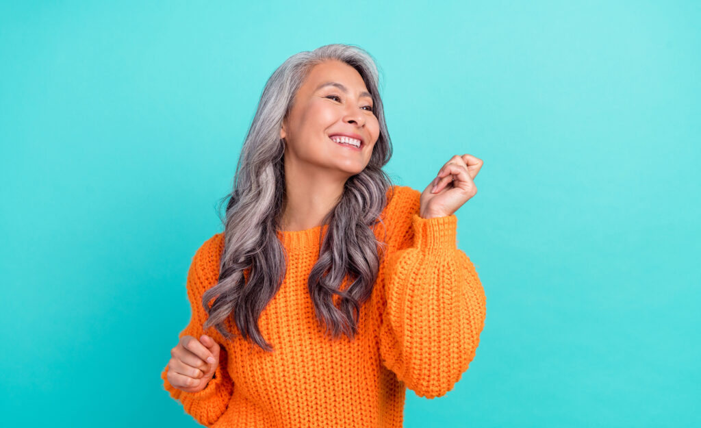 A highly sensitive woman in an orange knit dress smiling and dancing happily in front of a blue background